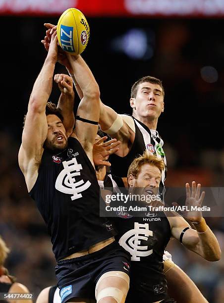 Mason Cox of the Magpies punches the ball away from Levi Casboult and Andrew Phillips of the Blues during the 2016 AFL Round 15 match between the...