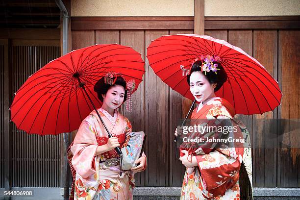 zwei geisha mädchen tragen kimonos unter rote sonnenschirme - geisha stock-fotos und bilder
