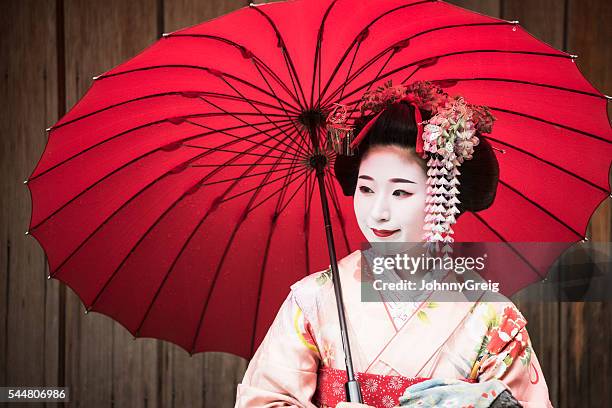 young japanese woman in traditional geisha clothing with red umbrella - geisha in training stock pictures, royalty-free photos & images