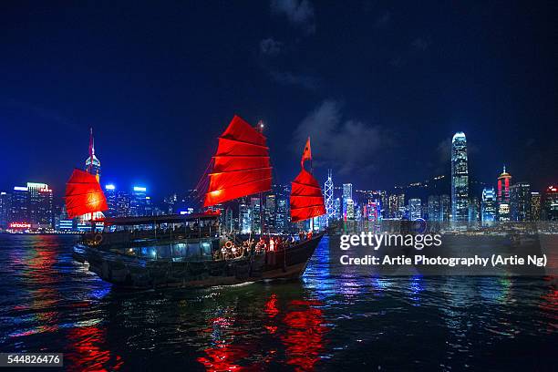 a traditional chinese junk sailing in victoria harbour with view of hong kong island skyline at night, hong kong, china - hong kong junk boat stock-fotos und bilder