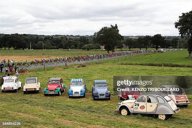 The pack rides past Citroen Deux Chevaux cars parked on a field during the 223,5 km third stage of the 103rd edition of the Tour de France cycling...