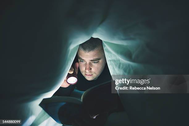 man reading book with flashlight - torch stock pictures, royalty-free photos & images