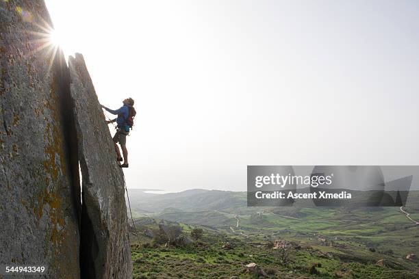 young man climbs steep rock, towards sunlight - great effort stock pictures, royalty-free photos & images