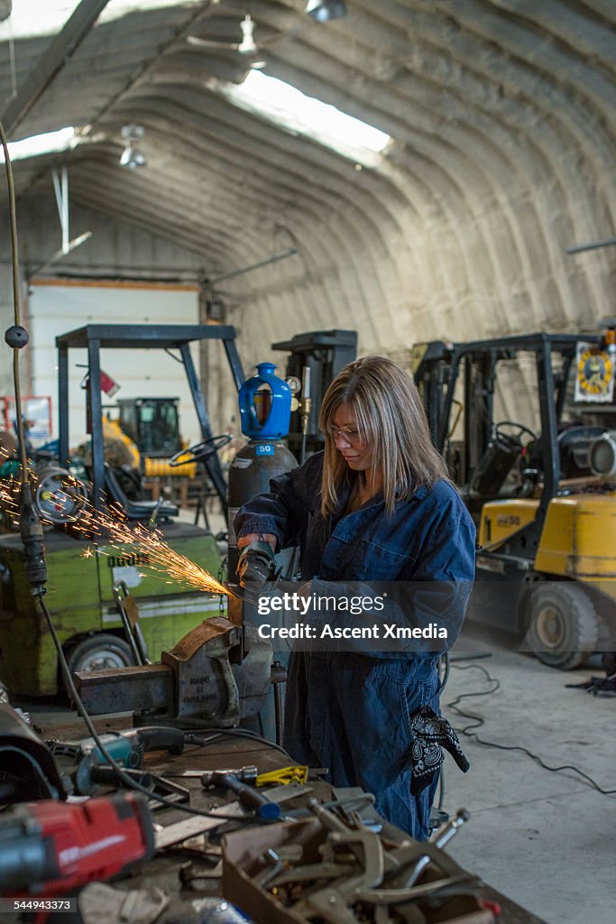Female metal worker grinds steel in workshop