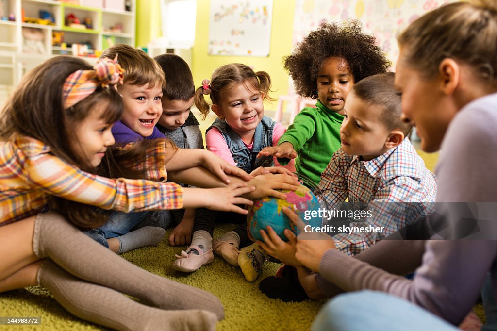 Playful kids and teacher gathering their hands on world globe.