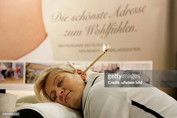 Deutschland, Berlin, Grüne Woche 2006. Wellness-Angebote: Trommelfellmasssage durch die Anwendung einer Ohrkerze. Das Verbrennen der rohrartigen...