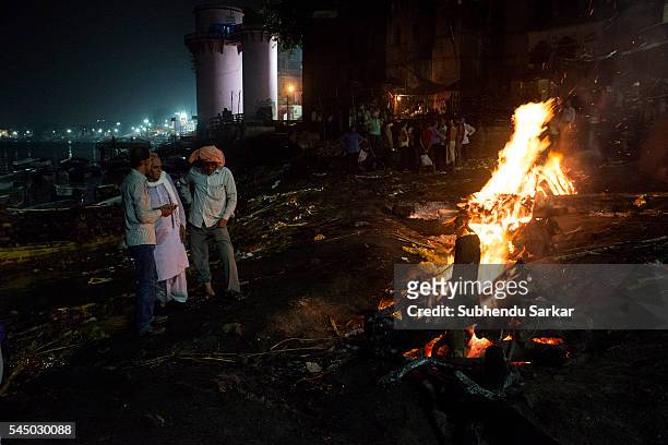 Relatives wait as a corpse is being cremated at Manikarnika ghat in Varanasi. It is a traditional holy place on the banks of river Ganges to cremate...