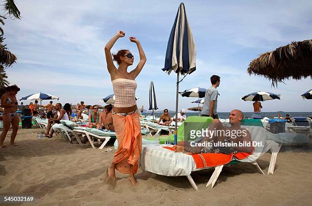 Spanien, Ibiza: Junge Leute feiern am Partystrand der Strandbar Bora Bora Disco Beach am Platja de en Bossa - junge Frau tanzt vor Mann im Liegestuhl.