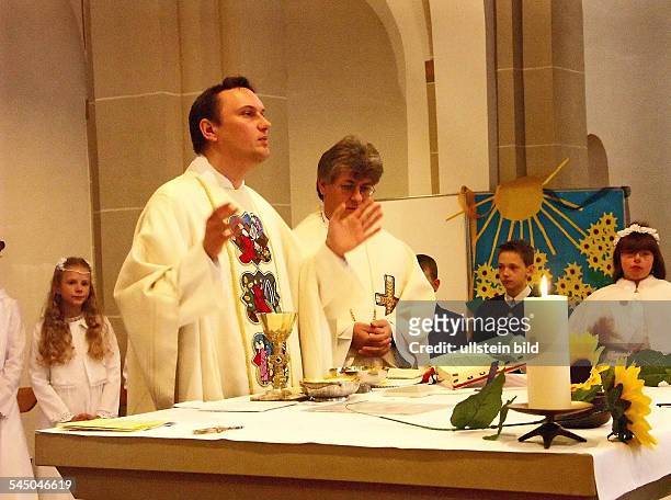Deutschland, Nordrhein-Westfalen, Koeln - Erstkommunion-Feier in einer katholischen Kirche. Die Messfeier wird von einem Kaplan geleitet, der von...