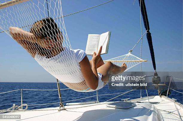 Segelurlaub, Segelturn. Junge Frau entspannt sich mit einem Buch in der Hängematte an Deck eines Segelbootes.