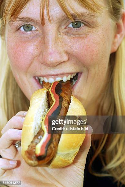 Frau ist eine Bratwurst im Brötchen mit Deutschlandsenf