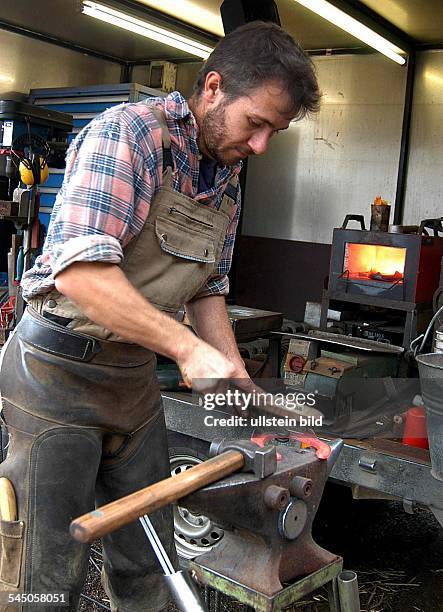 Handwerk, Hufschmiede, Hufschmied in der Werkstatt, Schmieden und Feilen eines Hufeisen auf dem Amboss.