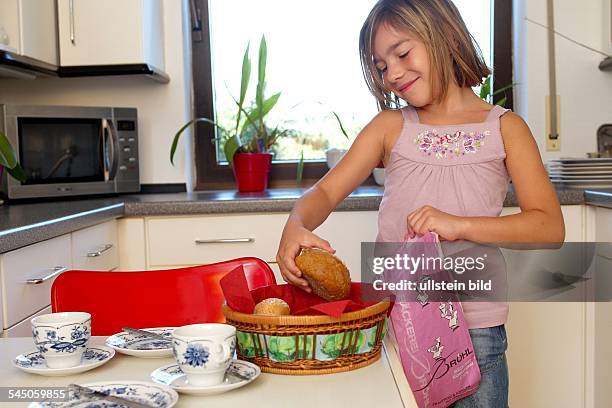 Deutschland, Mädchen deckt den Frühstückstisch und legt die Brötchen aus der Papiertüte in den Brotkorb