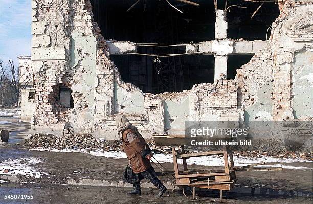 Frau mit Handkarren in Grosny voreinem zerstörten Gebäude.- 1996