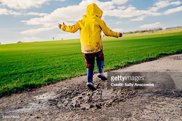 child jumping in a muddy puddle - yellow boot stock pictures, royalty-free photos & images