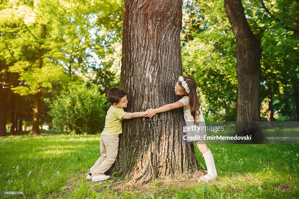 Irmão e irmã, segurando as mãos e abraçando árvore.