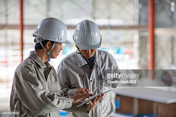 two engineers looking at a digital tablet at building site - construction meeting helmet stock pictures, royalty-free photos & images