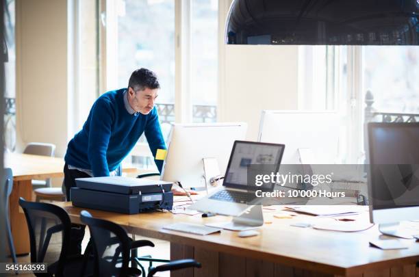 businessman standing by desk working on a computer - small business owners computer stock-fotos und bilder