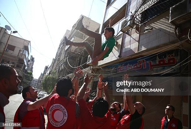 Members of the Syrian Arab Red Crescent throw a young boy under a psychological support program in the air in the rebel-held town of Douma, east of...