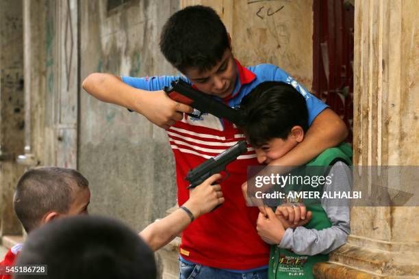 Syrian children play on a street with plastic toy guns in a rebel-held district of the northern city of Aleppo on July 6, 2016 during celebrations...