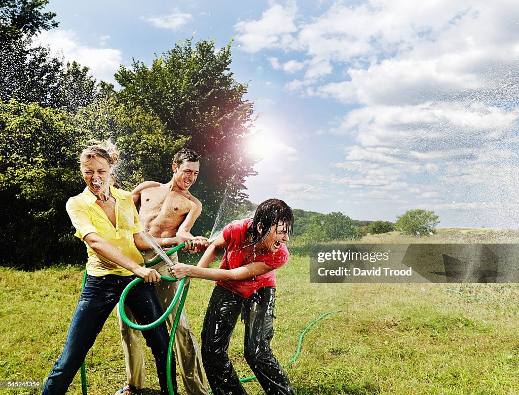 Young adults play with water hose