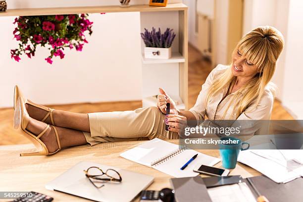 relaxed businesswoman polishing nails with feet up on the table. - nail file stock pictures, royalty-free photos & images