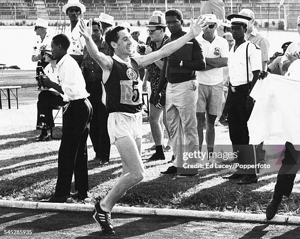 Scottish long distance runner Jim Alder smiles and raises his arms in the air as he crosses the finish line to win the marathon at the Commonwealth...