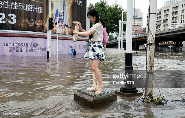This picture taken on July 6, 2016 shows a woman emptying the water from her boots at a flooded area in Wuhan, central China's Hubei province. Heavy...