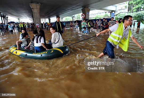 This picture taken on July 6, 2016 shows a rescuer helping people with an inflatable boat in flood water in Wuhan, central China's Hubei province....