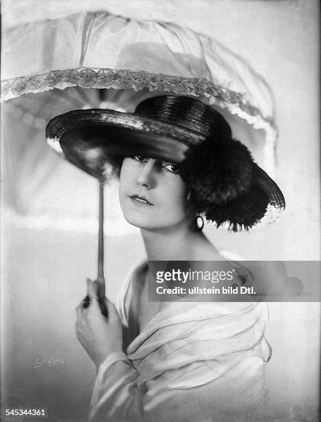 Mit einem Hut mit breiter Krempe die mit Pom-Poms geschmückt ist und einem Sonnenschirmveröffentlicht in Dame 13/1922Foto: Ernst Sandau