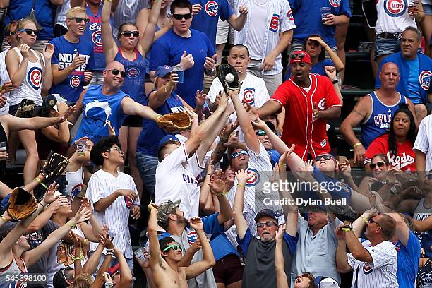 Fans reach to catch a home run ball from Javier Baez of the Chicago Cubs in the third inning against the Cincinnati Reds at Wrigley Field on July 5,...