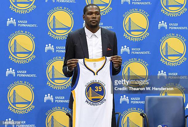 Kevin Durant of the Golden State Warriors poses with his new jersey during the press conference where he was introduced as a member of the Golden...