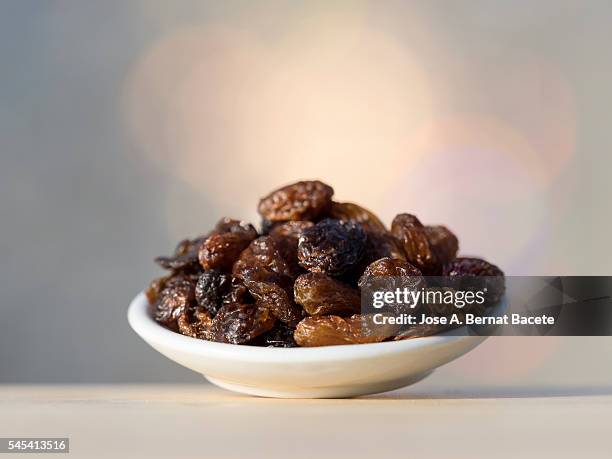 closeup of a plate of 	raisin  on a wooden table illuminated by sunlight - raisin stock-fotos und bilder