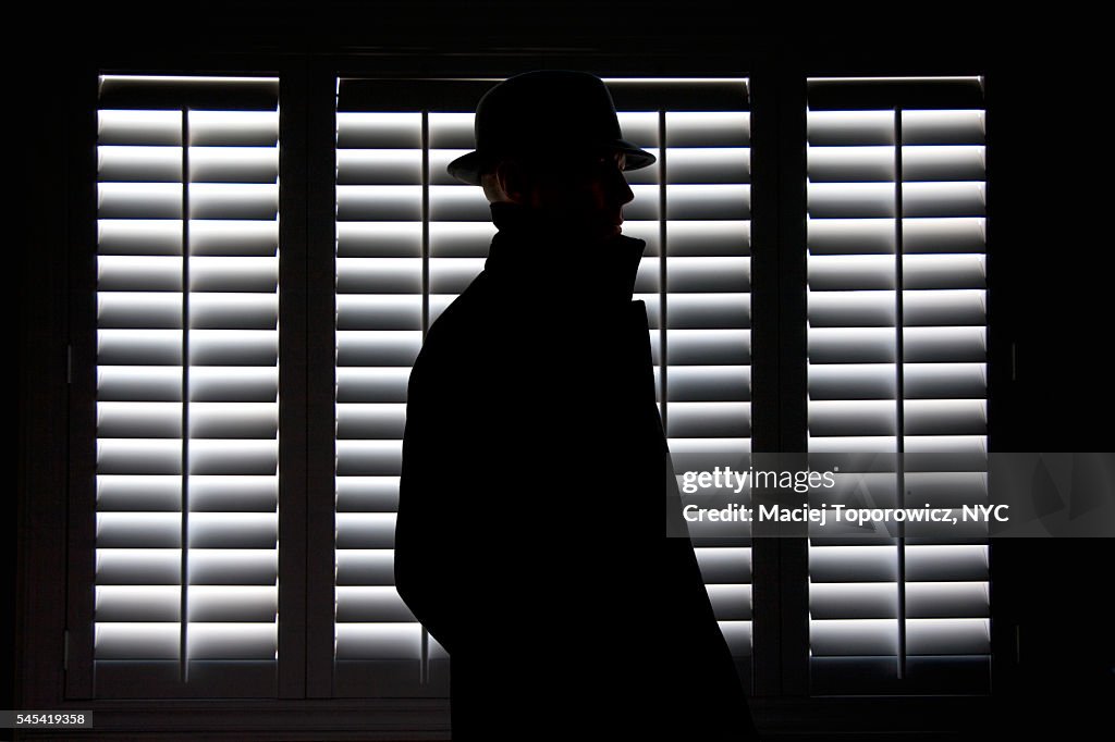 Silhouette of a man in hat against screen window.