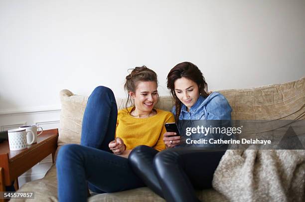 two friends looking at a cell phone - 2 young woman on couch stock pictures, royalty-free photos & images