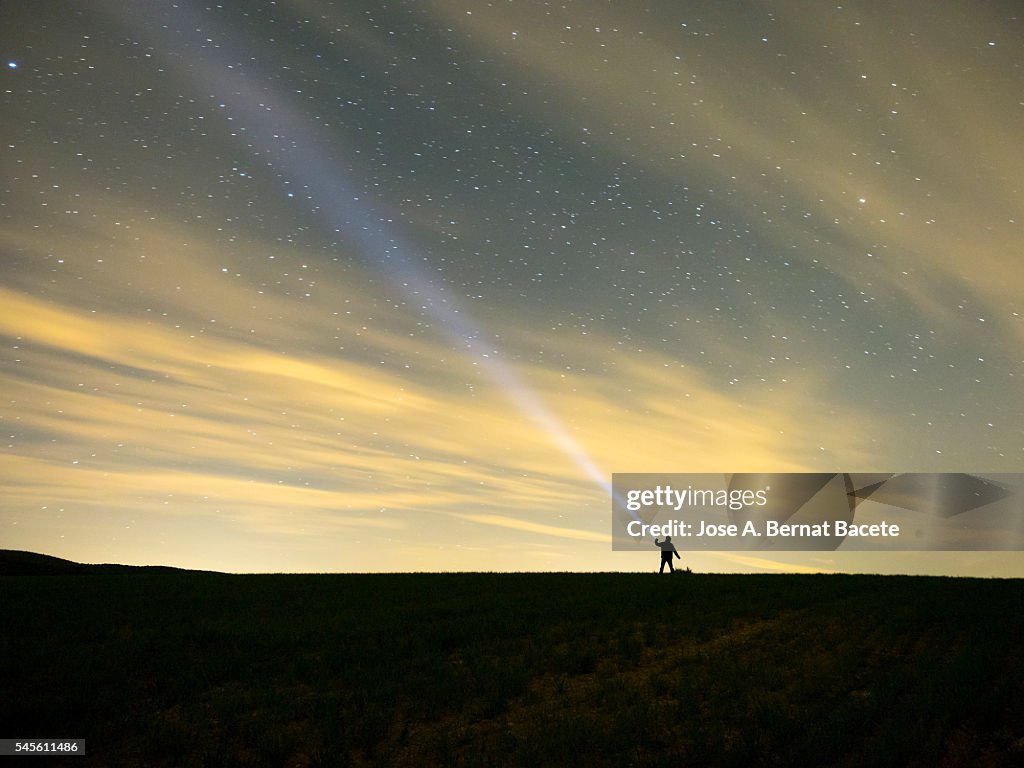 Silhouette of a man with a lantern projecting a bundle of light on the sky during the night in the field