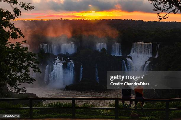 iguacu, brasilien: silhouette der touristen an den berühmten wasserfällen, beobachten einen dramatischen sonnenuntergang über den wasserfällen in der nähe des teufels kehle - foz do iguacu stock-fotos und bilder