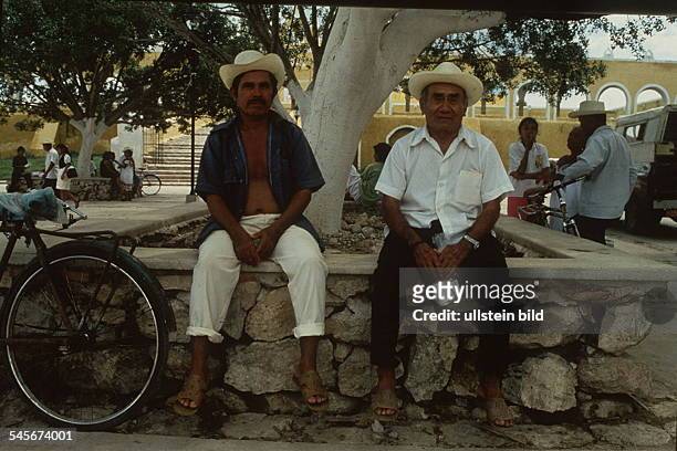 Zwei Mexikaner mit Strohüten sitzen imSchatten eines Baumes.- 1993