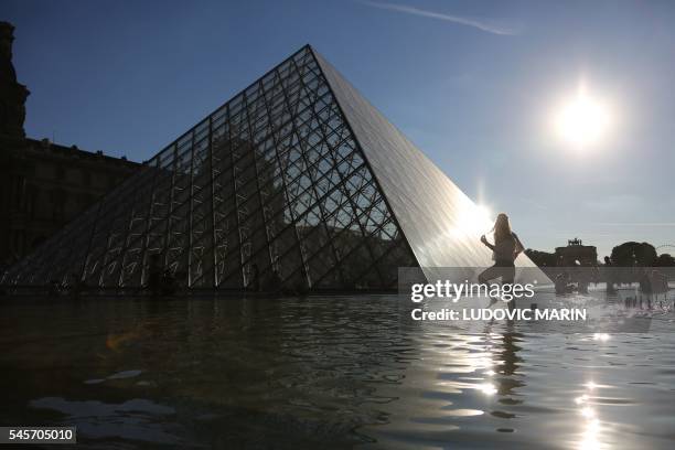 Person stands in water at a fountain near the Louvre pyramid at sunset in Paris on July 9, 2016. / AFP PHOTO / LUDOVIC MARIN