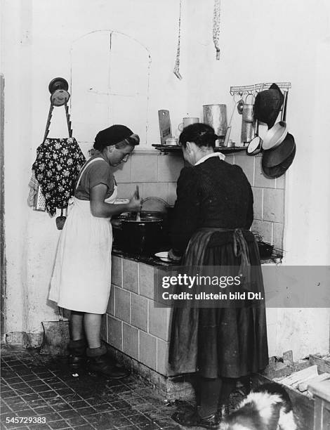 Eine Arbeitsmaid, die in der Nähe vonIglau eingesetzt ist, hilft einer Bäuerinbeim Kochen- veröffentlicht März 1942