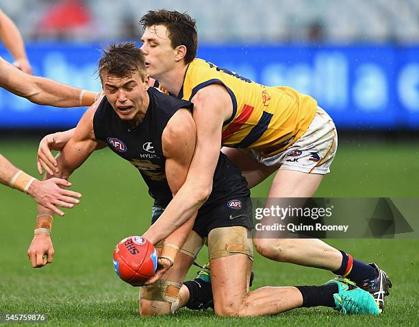 Patrick Cripps of the Blues handballs whilst being tackled Jake Lever of the Crows during the round 16 AFL match between the Carlton Blues and the...