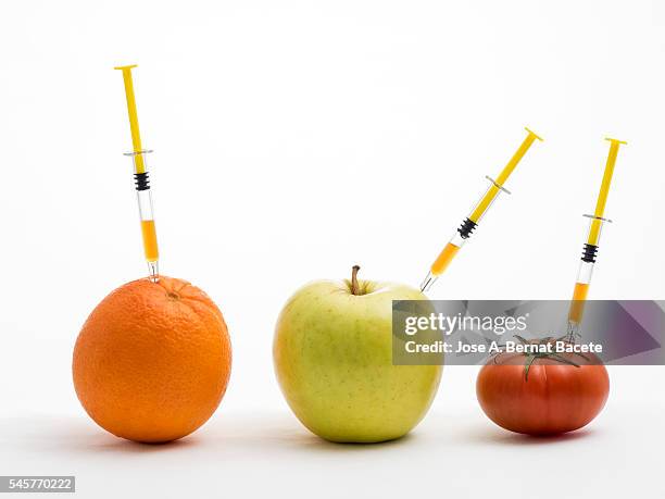 orange, apple and tomato with a syringe stuck concept of transgenic foods - modificación genética fotografías e imágenes de stock