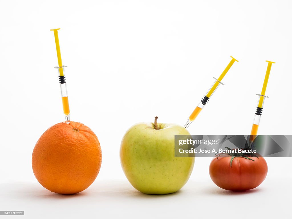 Orange, apple and tomato with a syringe stuck concept of transgenic foods