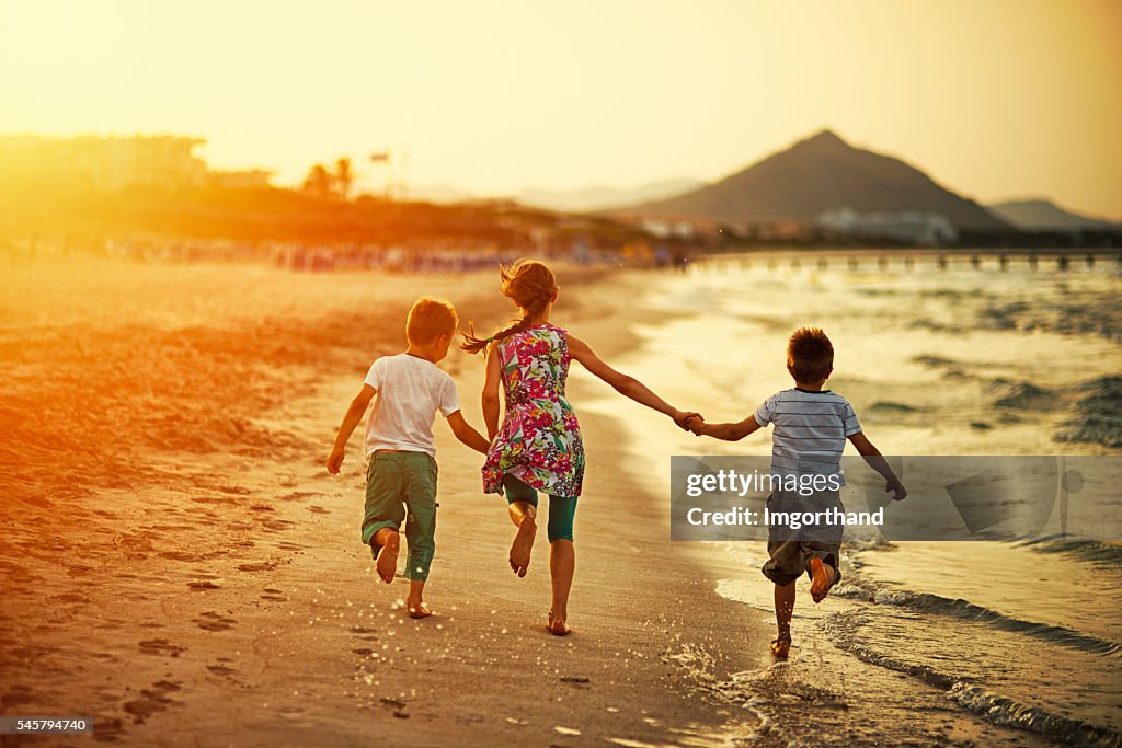 Frères et sœur courant sur la plage au coucher du soleil