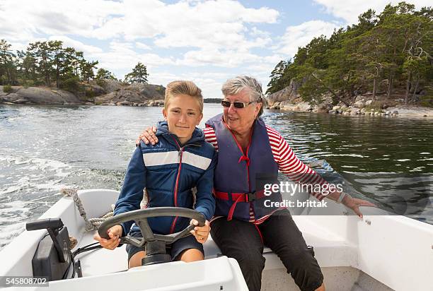 proud young captain running small motor boat with grandmother. - motorboat stock pictures, royalty-free photos & images
