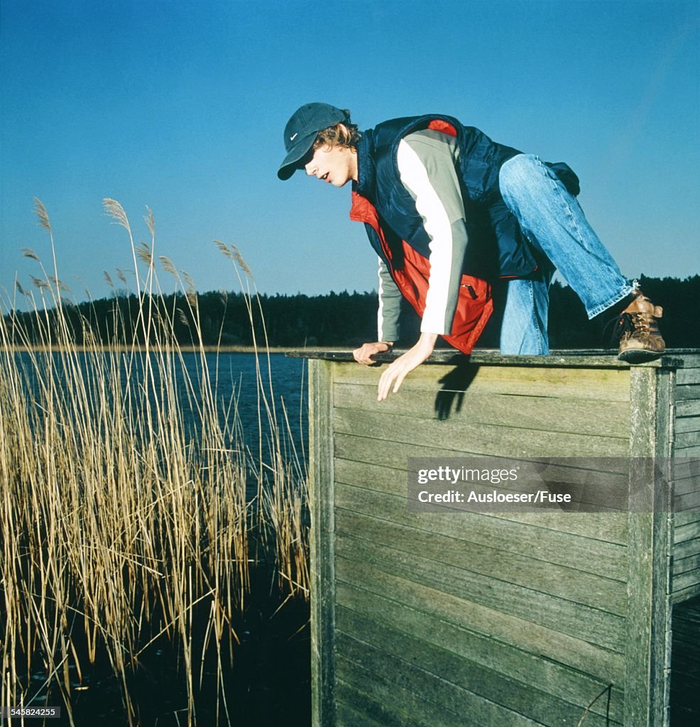 Young man climbing above wooden barrier by a lake