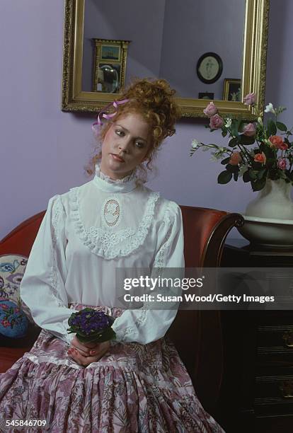 Portrait of an unidentified model in a Victorian-style blouse as she sits on a couch, a flower bouquet in her hands, December 1977. The photo was...