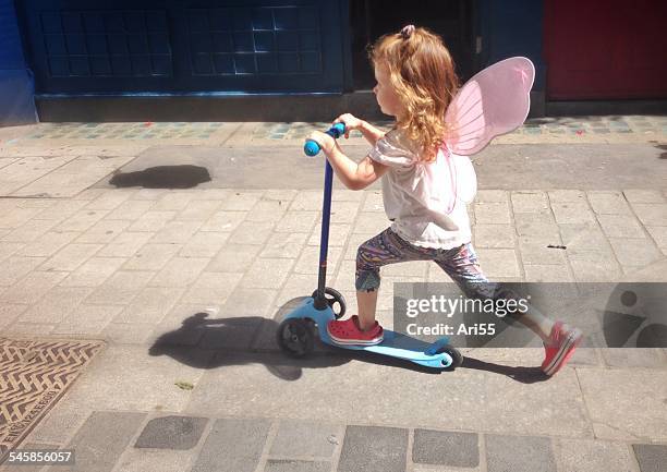 uk, england, london, portrait of girl (2-3) with fairy wings riding scooter on city pavement - scooter stock pictures, royalty-free photos & images