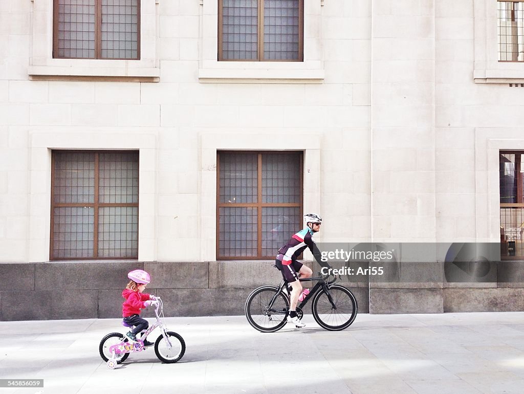 UK, England, London, Father and daughter cycling past building