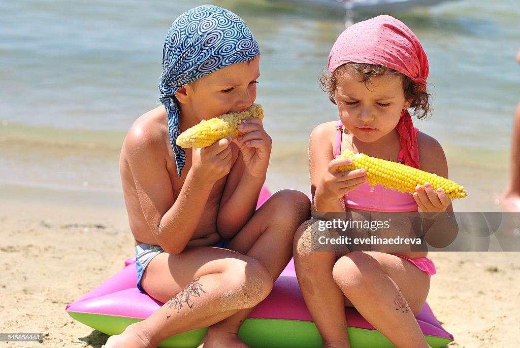 Portrait of girl (2-3) and boy (4-5) eating sweetcorn on beach